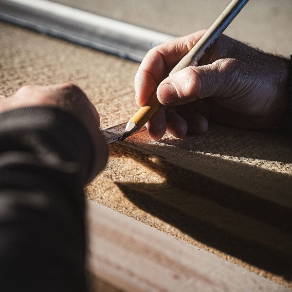 Eine Person zeichnet mit einem Bleistift und einem Lineal bei natürlichem Licht eine gerade Linie auf ein Stück Holz.
